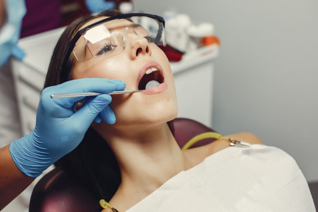 The dentist treats the girl's teeth. A young woman visited a dentist. The doctor works with an assistant
